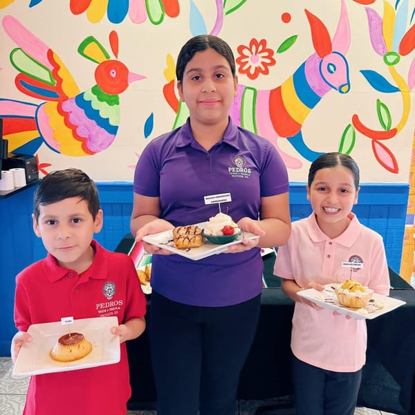 Three people, two children and one adult, hold plates of desserts in front of a colorful mural.