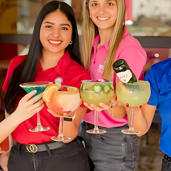 Smiling women holding various margaritas, including a blue one, a fruit-garnished one, and a jalapeño one.